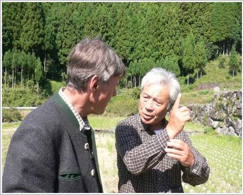Der 70-jhrige Reisbauer Shunji Koyama erklrt dem Gast aus Deutschland das Prinzip Satoyama: Landnutzung in Harmonie mit der Natur. Der Hangwald im Hintergrund besteht aus Lebensbumen und Japanischen Sicheltannen.